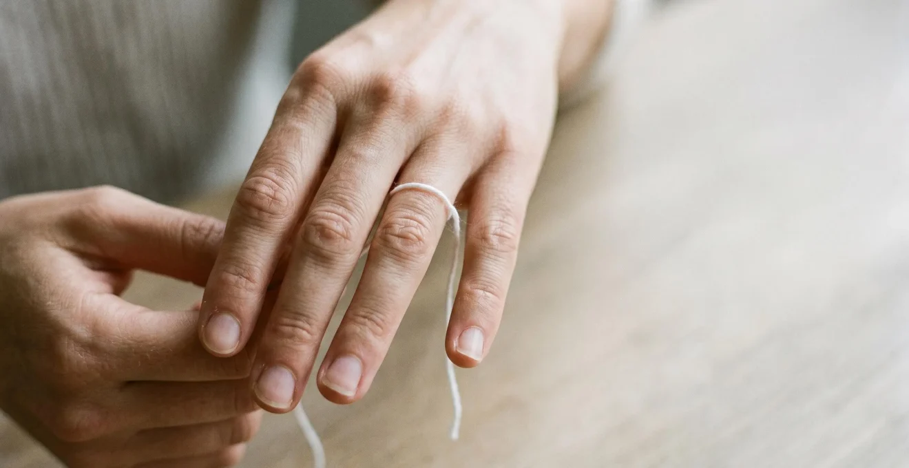 Main féminine avec ficelle blanche enroulée autour de l'annulaire pour mesurer le tour de doigt