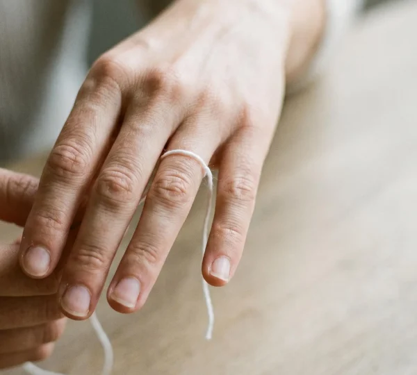 Main féminine avec ficelle blanche enroulée autour de l'annulaire pour mesurer le tour de doigt