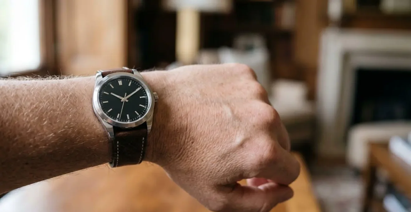 Poignet masculin portant une montre de luxe en acier inoxydable avec cadran noir et bracelet en cuir, photographié dans un environnement élégant aux tons neutres