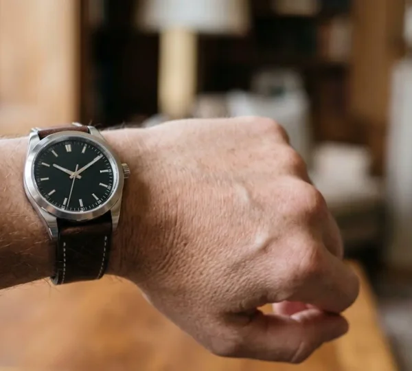 Poignet masculin portant une montre de luxe en acier inoxydable avec cadran noir et bracelet en cuir, photographié dans un environnement élégant aux tons neutres